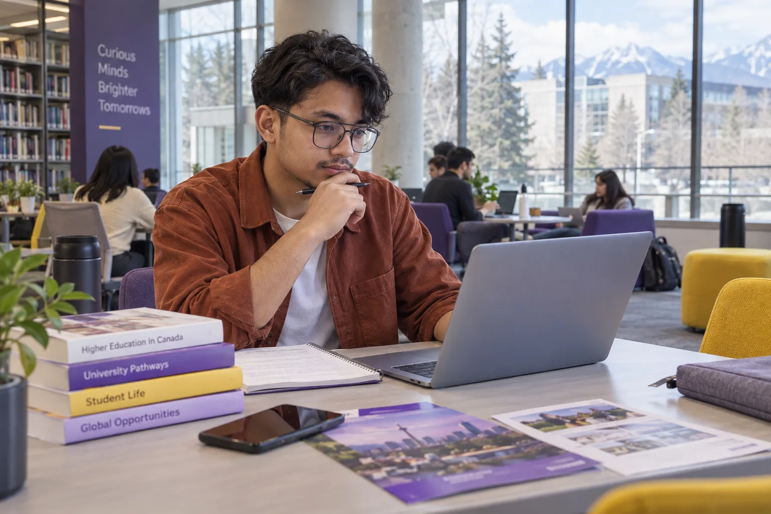 Young Nepali man with glasses comparing Canadian university courses and intake options using a laptop and notebook for Canada study planning