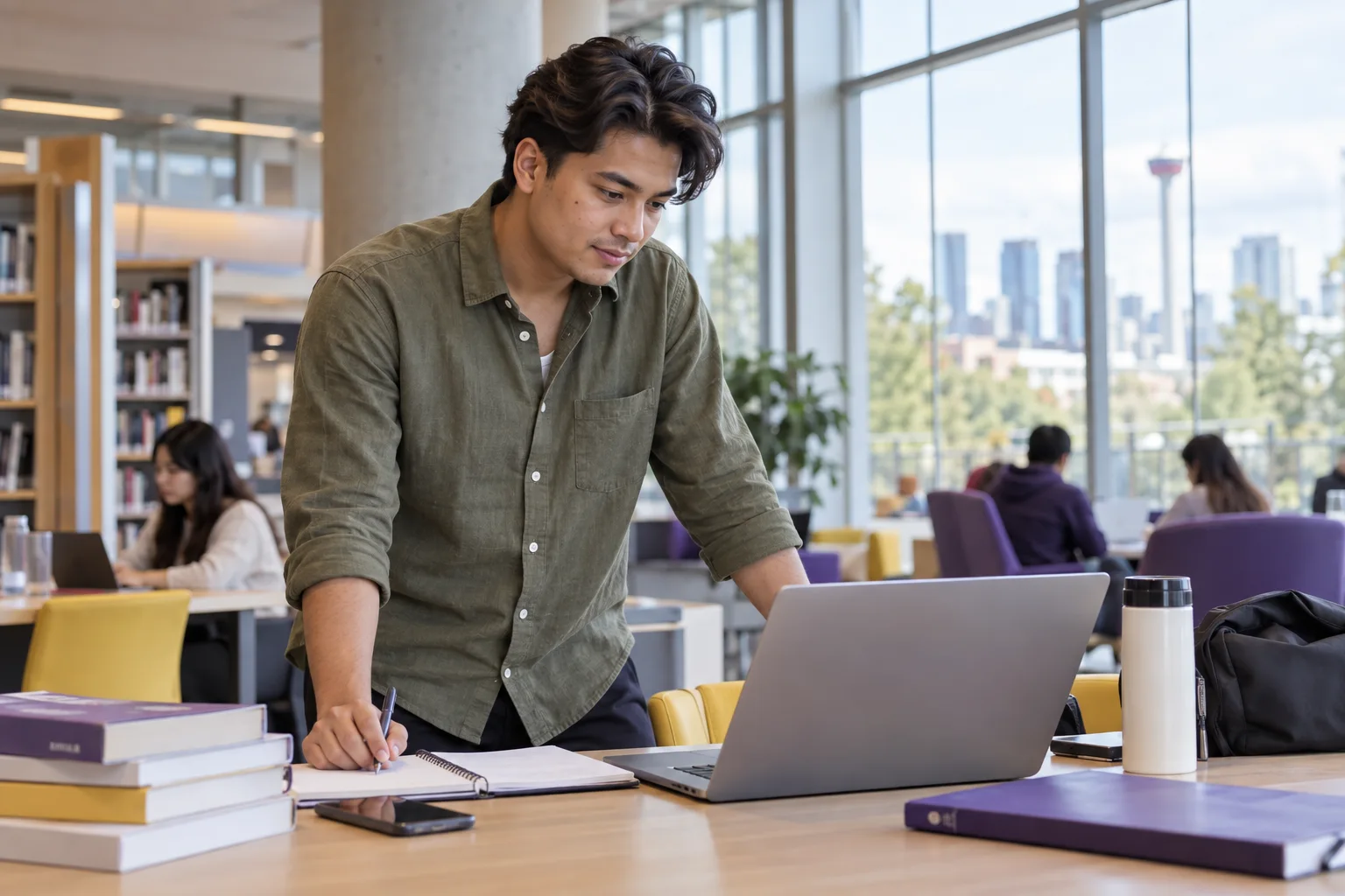 Young Nepali man with swept-back hair comparing Canadian university courses and intake options using a laptop and notebook for Canada study planning