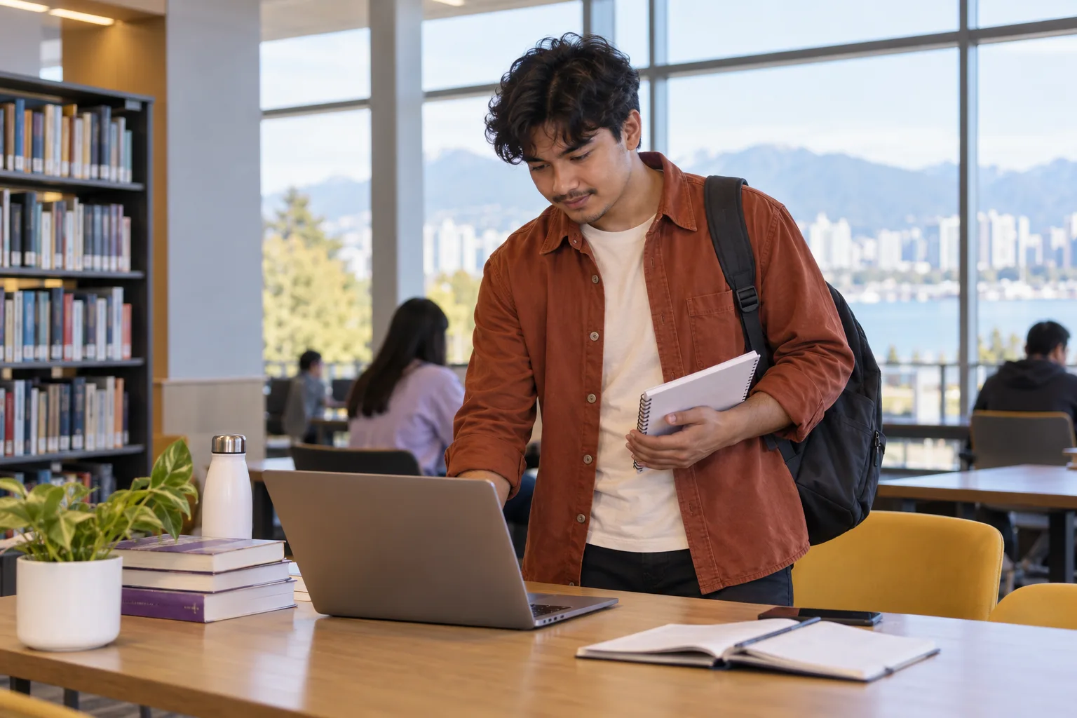 Young Nepali man with wavy hair planning student accommodation and everyday campus life with a notebook and laptop in a welcoming Canada study setting for Canada study planning