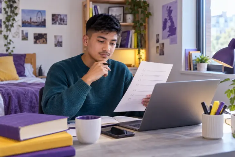 Young Nepali man with cropped hair reviewing an unbranded study application document checklist with a laptop for UK study planning.